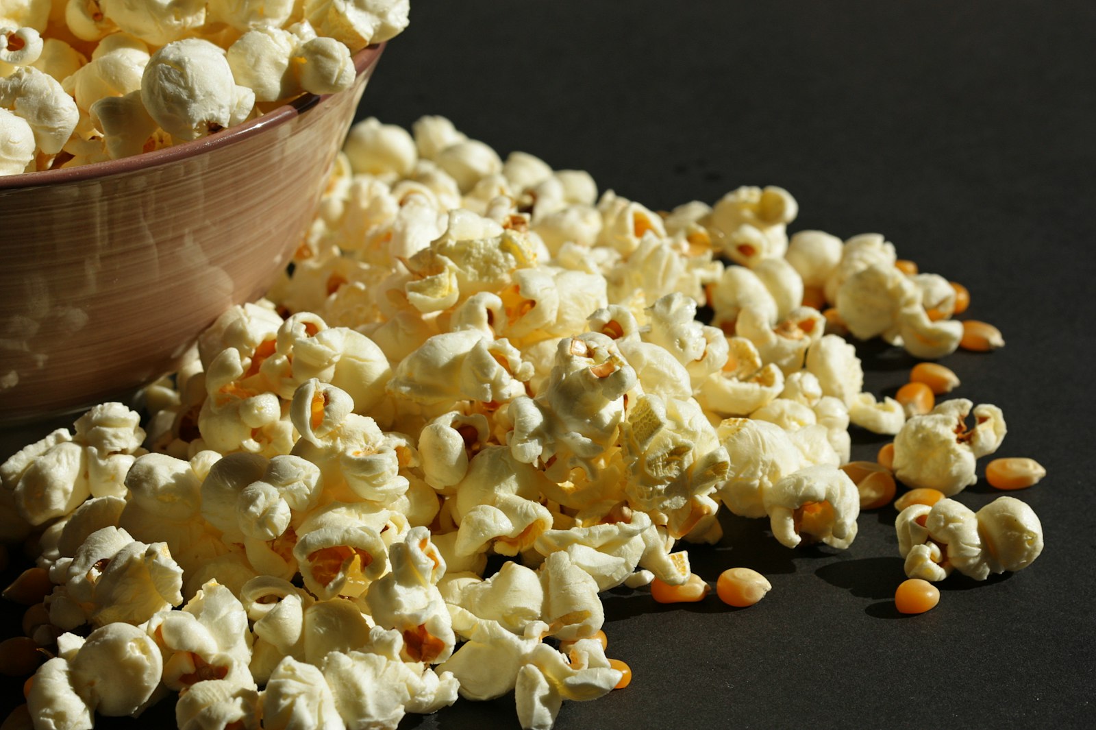 Popcorn spilling from a bowl with raw kernels